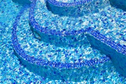 water lapping over blue mosaic tiles on the steps of a cool and inviting swimming pool