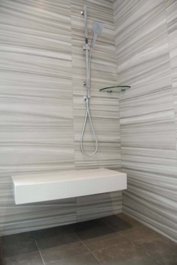 modern striped tile in neutral tones lines the shower walls and contrasts the rich brown floor tile