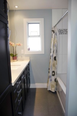 Dark cabinets set against quaint blue walls are tied together with a flower patterned shower curtain.