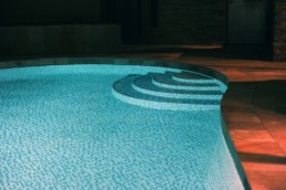 Night time view of the swimming pool steps and partial shallow end, finished in a glass mosaic tile