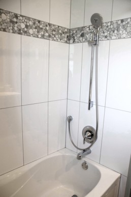 A pebbled tile in cool grey tones accents the white shower walls.